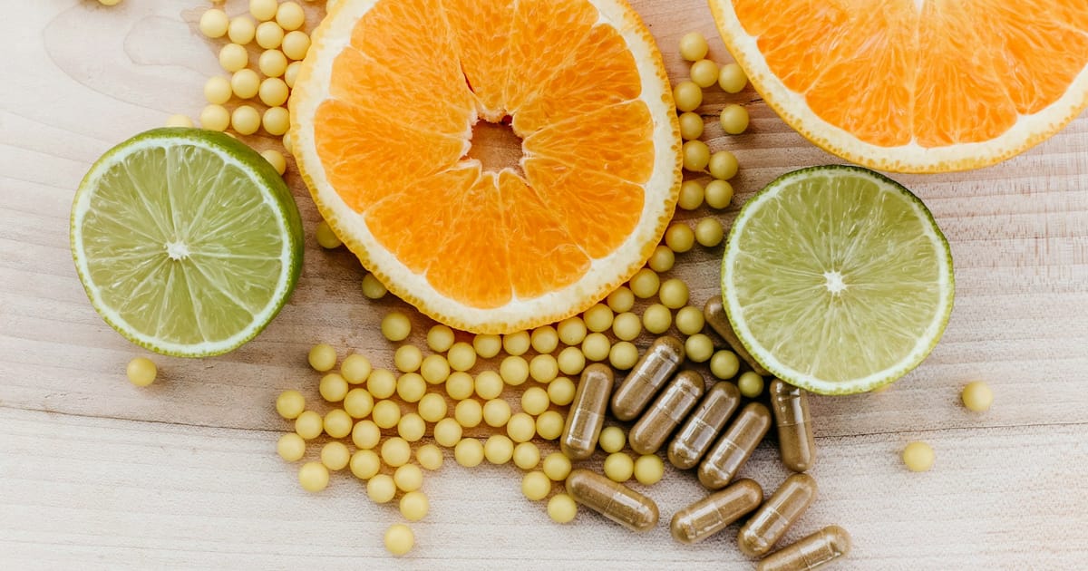 Rodajas de cítricos junto a cápsulas y perlas de suplementos sobre una superficie de madera.
