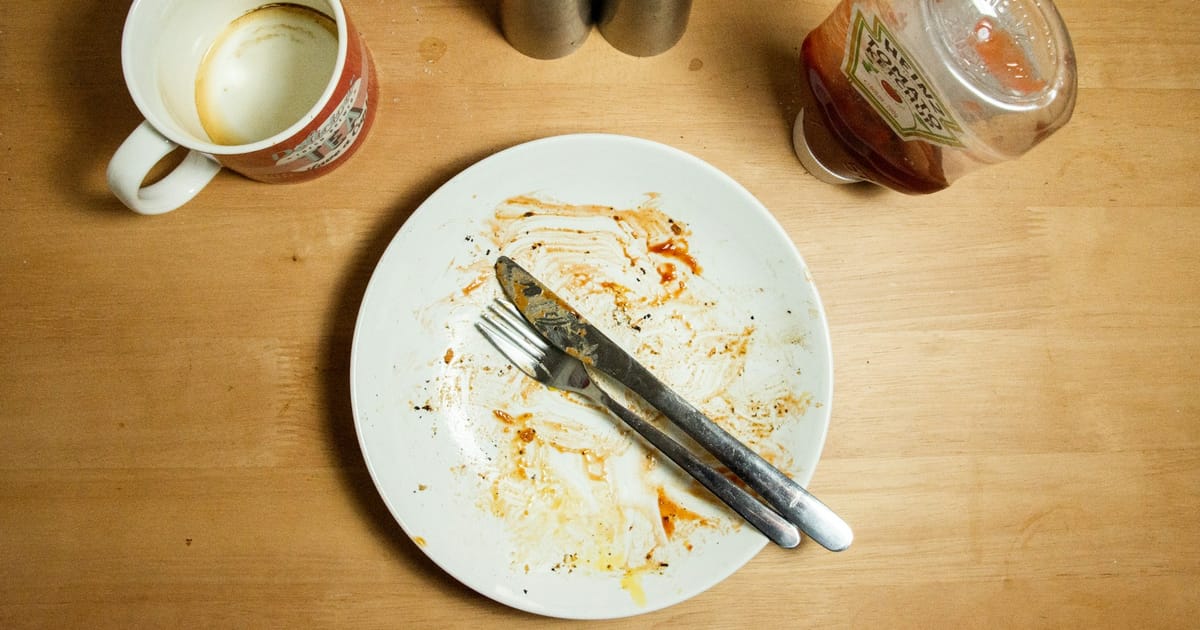 Un tenedor y un cuchillo de acero inoxidable sobre un plato blanco vacío.