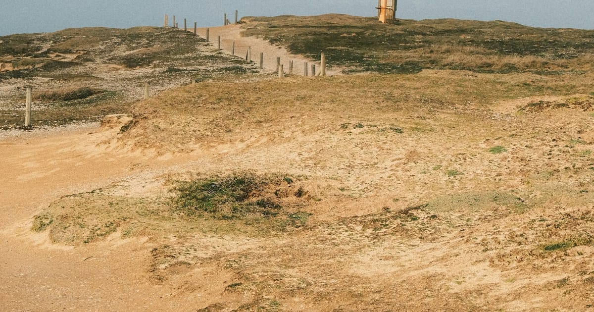 Una persona camina por un sendero de tierra en un paisaje abierto.