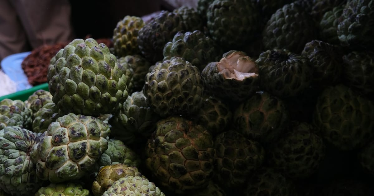 Frutas verdes de cáscara gruesa apiladas en un puesto de mercado.