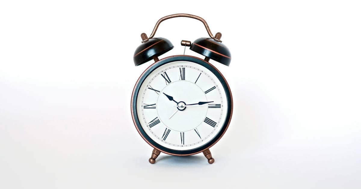 Un reloj despertador analógico de campanas sobre un fondo blanco.