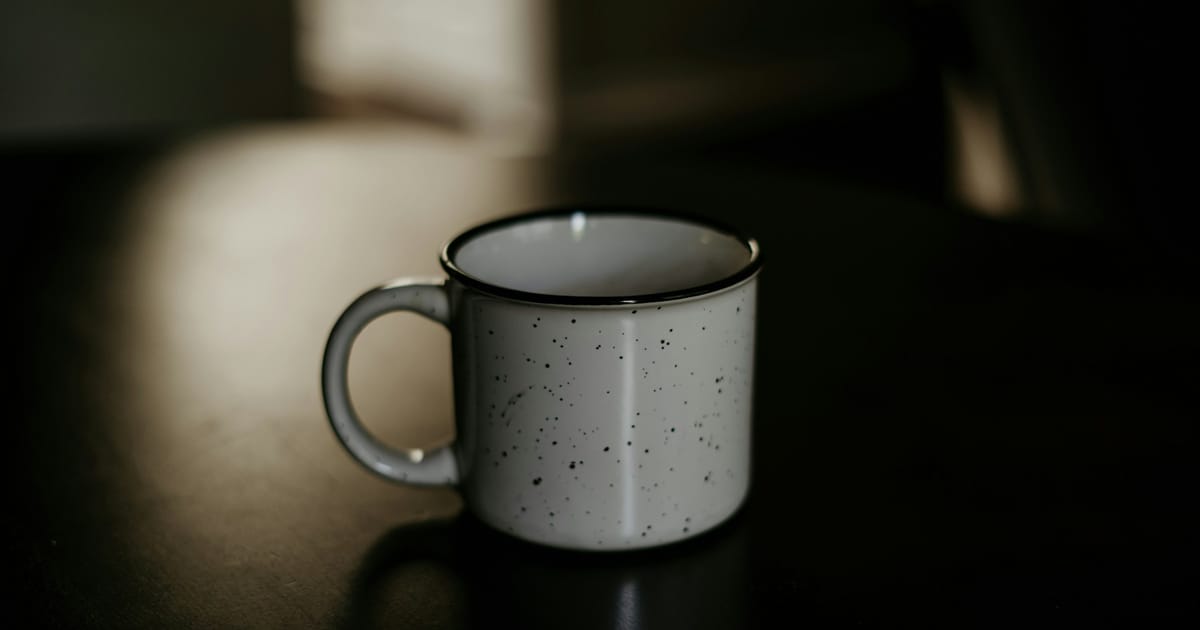 Una taza de café blanca y negra sobre una superficie oscura.
