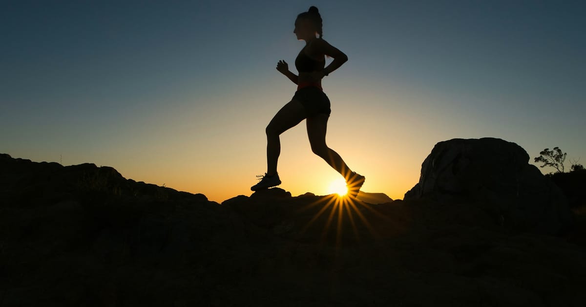 La silueta de una mujer corriendo por un sendero de roca al atardecer.