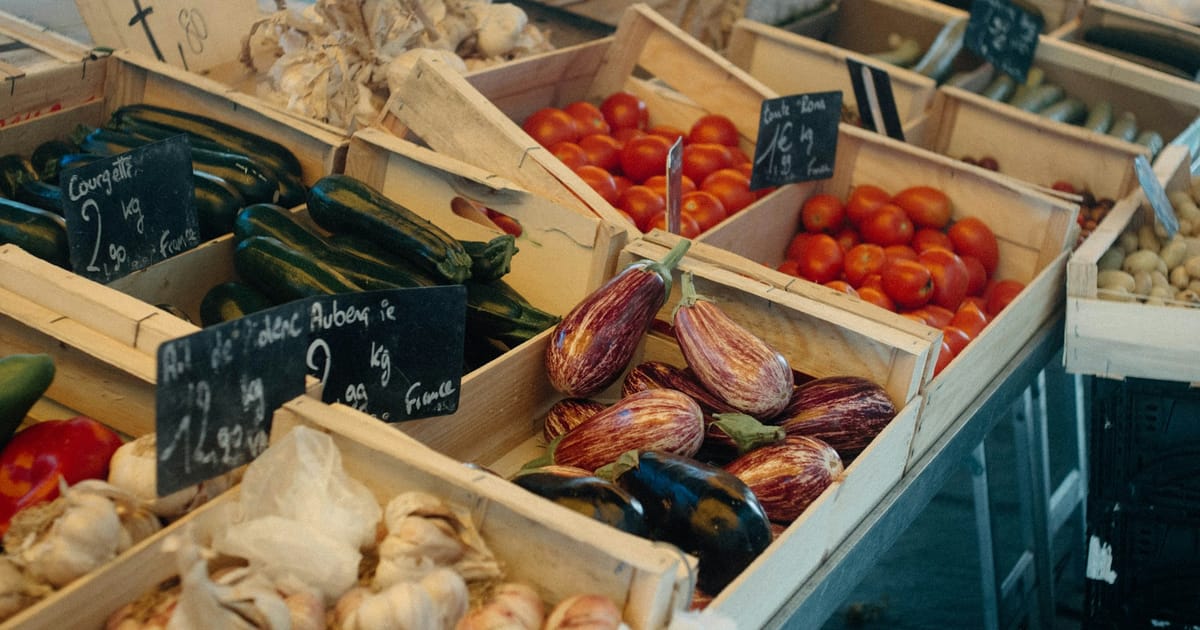 Cajones de madera con verduras frescas de distintos colores en un mercado.