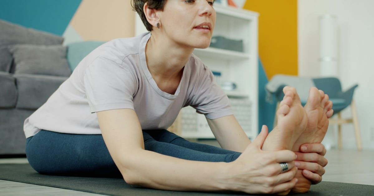 Una mujer estirando las piernas sobre una esterilla de yoga.