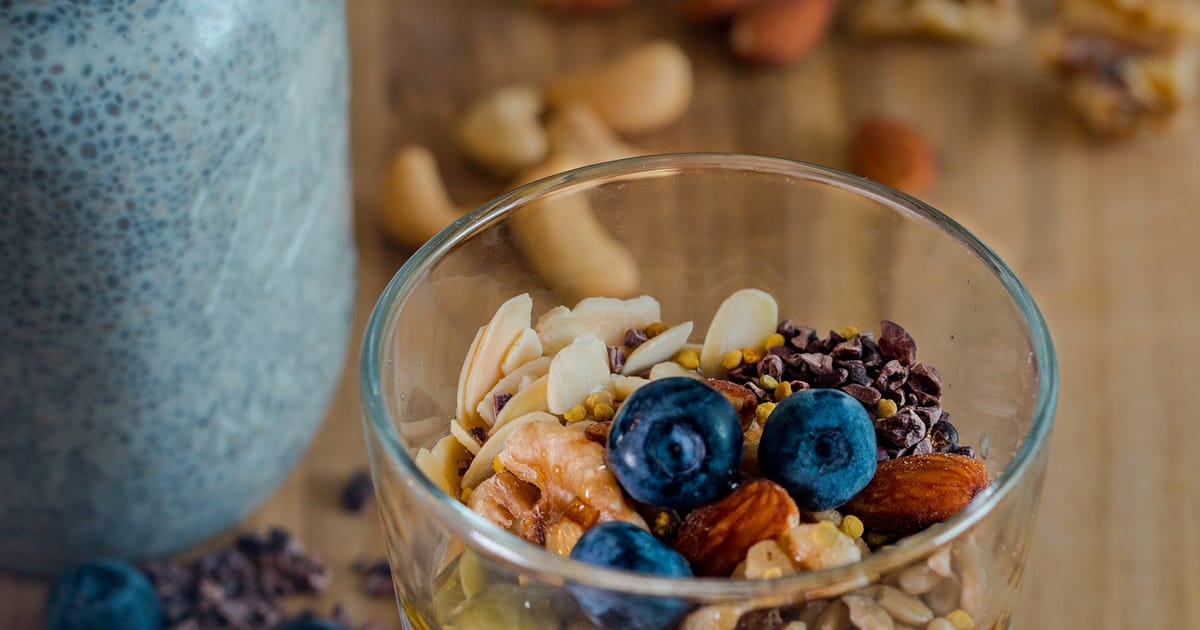 Un frasco de chía hidratada junto a un vaso con frutos secos y arándanos.