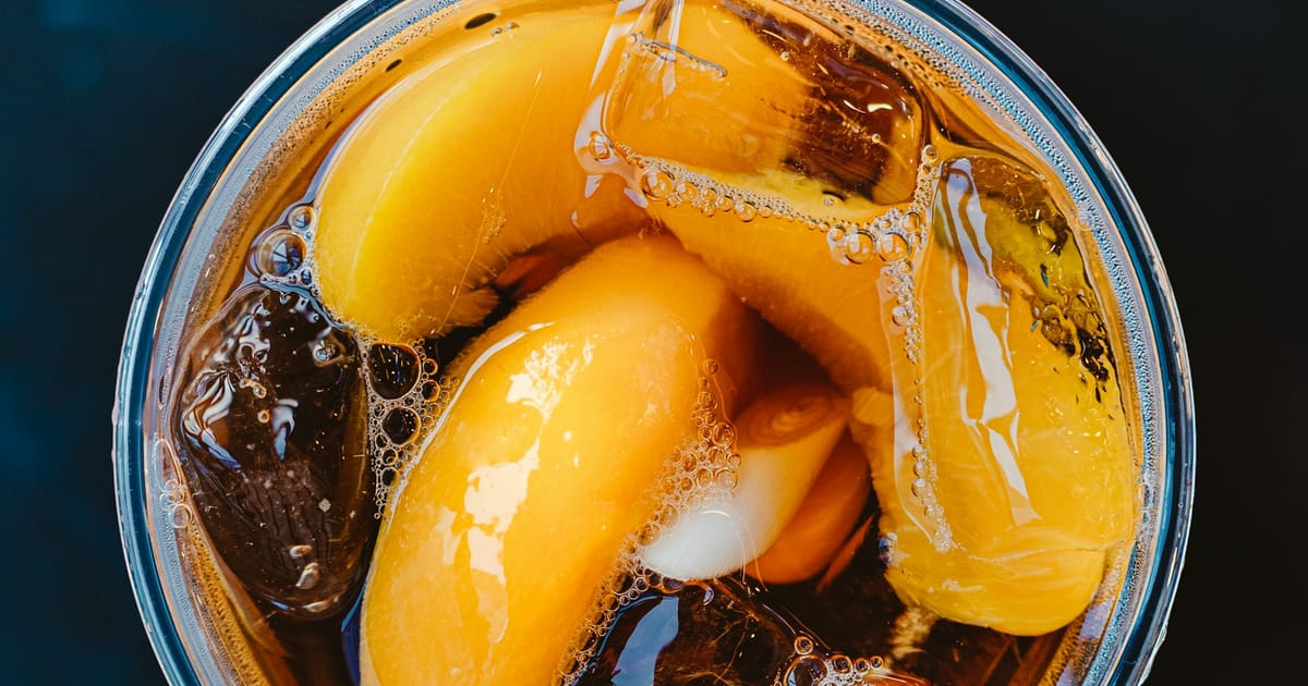 Un vaso con una bebida color ámbar, hielo y mitades de durazno.