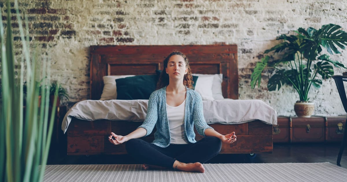 Una mujer sentada con las piernas cruzadas en el suelo, en una postura de meditación tranquila.