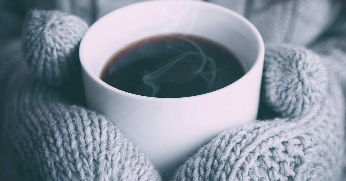 Una persona sostiene con las dos manos una taza de bebida caliente.